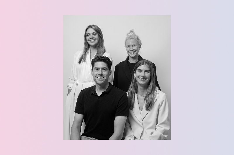 A black and white portrait of four smiling people arranged in a casual group pose.